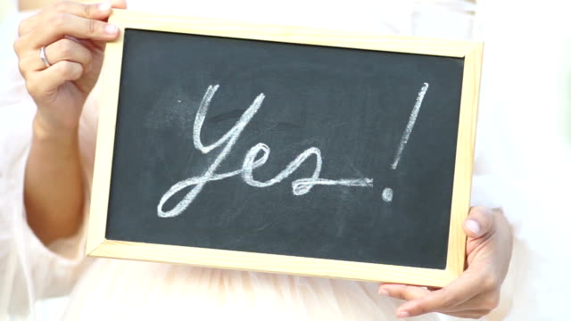 Wedding concept. Word “Yes” written on blackboard shown by young women.