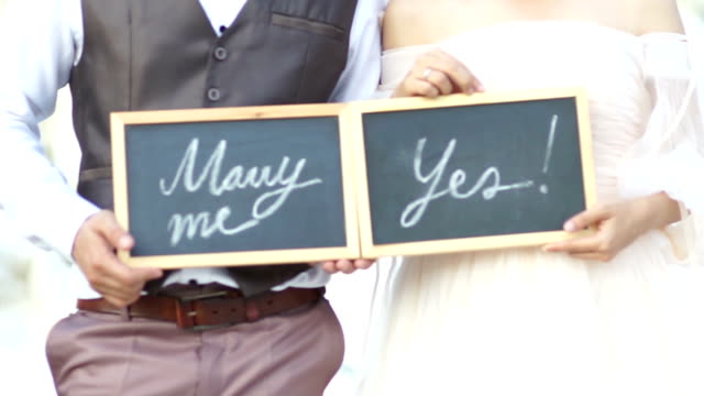 Wedding concept. Will you marry me question and yes, handwritten on blackboard shown by the wedding couple.