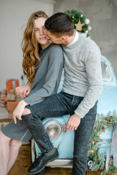 Young caucasian couple sitting on retro car in christmas decorated studio stock photo