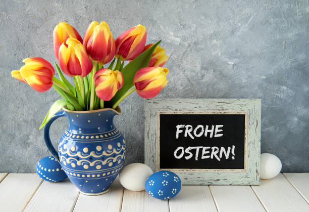 istock Red-yellow tulips in blue ceramic pitcher with Easter eggs and a blackboard on gray background 915850224