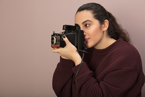 Young woman photographer taking a photo with a vintage camera she focuses on her subject in a side view