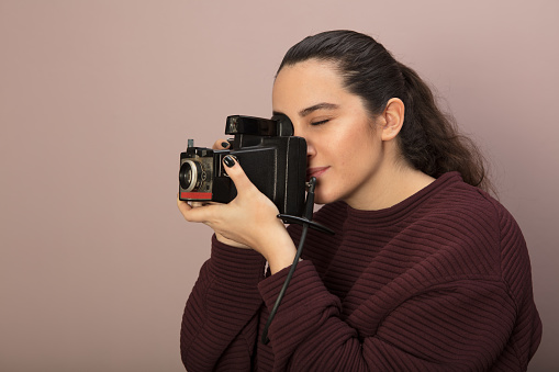 Female photographer taking a photo with a vintage camera she focuses on her subject in a side view