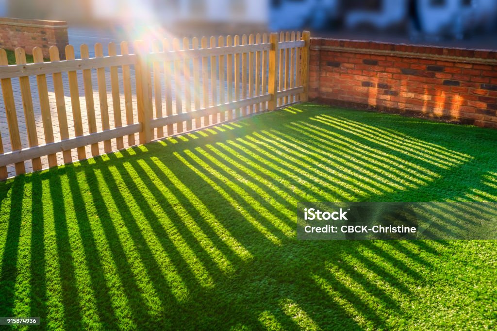 soleil qui brille à travers une palissade en bois sur une pelouse de gazon artificiel - Photo de Artificiel libre de droits