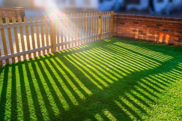 sun shining through a wooden picket fence onto an artifical grass lawn sunshine creating lens flare through a wooden picket fence in a front yard, front garden with artifical grass as a lawn and a red brick perimiter wall. artifical grass stock pictures, royalty-free photos & images