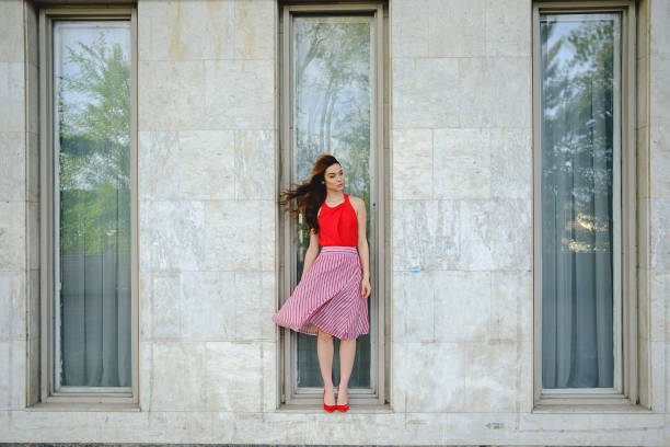 Gorgeous woman with flying hair and fluttering skirt in the wind posing while standing on a window like in a vitrine. Fashion, presenting clothes concept