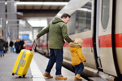 Little boy and his father go in express train on railway station platform. Travel, tourism, winter vacation and family concept. Man and his son together.