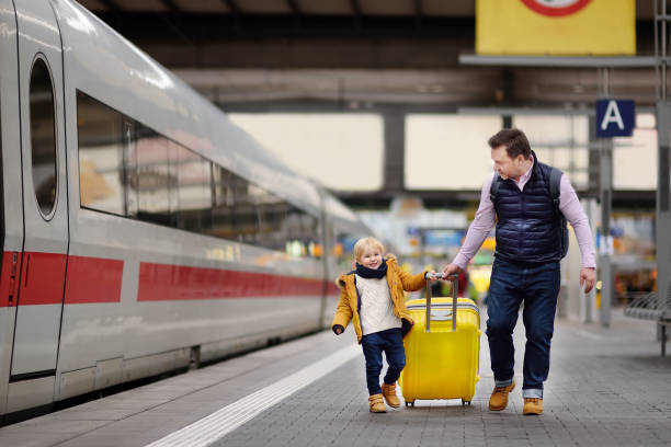 niño sonriente y su padre espera el tren en el andén de la estación - estación de tren fotografías e imágenes de stock
