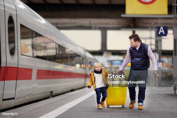 Photo libre de droit de Sourire De Petit Garçon Et Son Père Attend Un Train Express Sur Le Quai De La Gare Ferroviaire banque d'images et plus d'images libres de droit de Famille