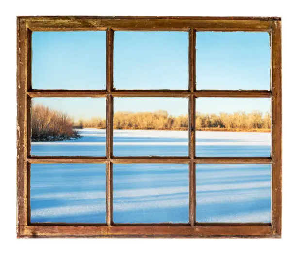 frozen lake with long tree shadows as seen  through vintage, grunge, sash window with dirty glass