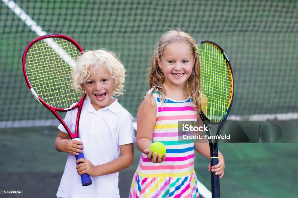 Children playing tennis on outdoor court Boy and girl playing tennis on outdoor court. Kids with tennis racket and ball in sport club. Active exercise. Summer activities for children. Training for young kid. Child learning to play. Tennis Stock Photo