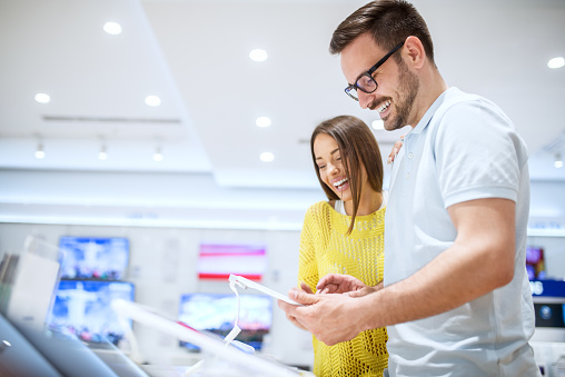 Charming young smiling love couple looking on a tablet while buying in a tech store.