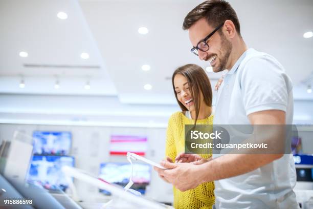 Charming Young Smiling Love Couple Looking On A Tablet While Buying In A Tech Store Stock Photo - Download Image Now