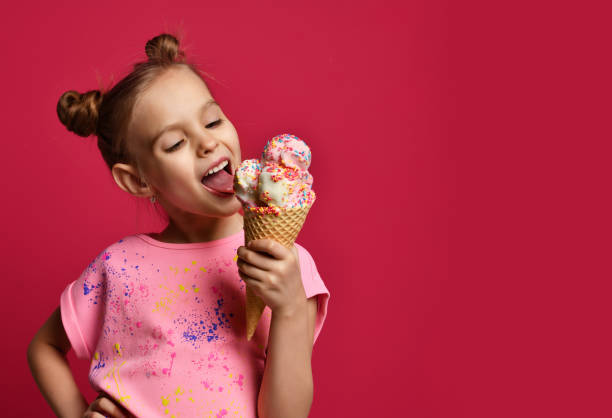 Pretty baby girl kid eating licking big ice cream in waffles cone with raspberry happy laughing stock photo