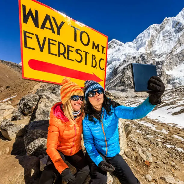 Young women taking selfie in Himalayas, next to the signpost "Way to Mount Everest Base Camp" . One of them, wearing blue jacket, is holding a digital tablet and the second woman is wearing orange jacket. Mount Everest National Park. This is the highest national park in the world, with the entire park located above 3,000 m ( 9,700 ft). This park includes three peaks higher than 8,000 m, including Mt Everest. Therefore, most of the park area is very rugged and steep, with its terrain cut by deep rivers and glaciers. Unlike other parks in the plain areas, this park can be divided into four climate zones because of the rising altitude. The climatic zones include a forested lower zone, a zone of alpine scrub, the upper alpine zone which includes upper limit of vegetation growth, and the Arctic zone where no plants can grow. The types of plants and animals that are found in the park depend on the altitude.
