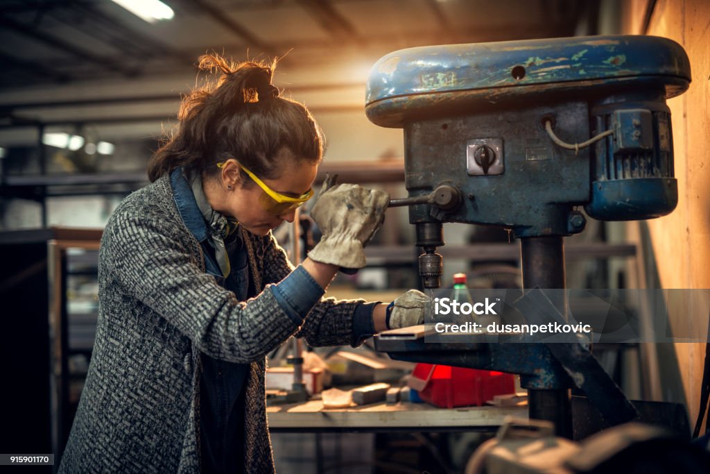 Portrait view of focused serious middle aged professional female carpentry working with an electric drill in the workshop. Carpenter Stock Photo