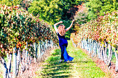 Elegant young woman in blue velvet dress by vineyard winery grapevine leaves red dry green in Virginia, back