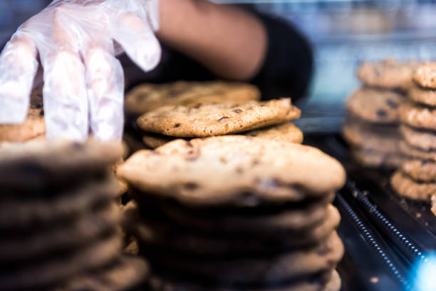 istock Closeup of chocolate chip cookies on display in bakery pile stack with employee worker baker glove on hand touching baked goods sweets 915908112