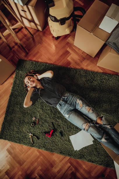 junge frau umzug in eine neue wohnung. anhören von musik auf einem teppich liegend - carpet floor lying down people stock-fotos und bilder