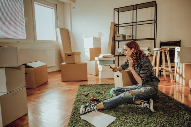 istock Young woman moving to a new apartment. Typing a message while sitting down on a carpet 915914876