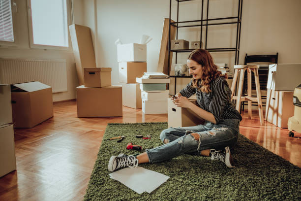 istock Young woman moving to a new apartment. Typing a message while sitting down on a carpet 915914878
