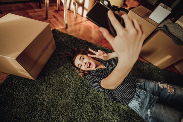 junge frau umzug in eine neue wohnung. nehmen eine selfie liegend auf einem teppich - carpet floor lying down people stock-fotos und bilder