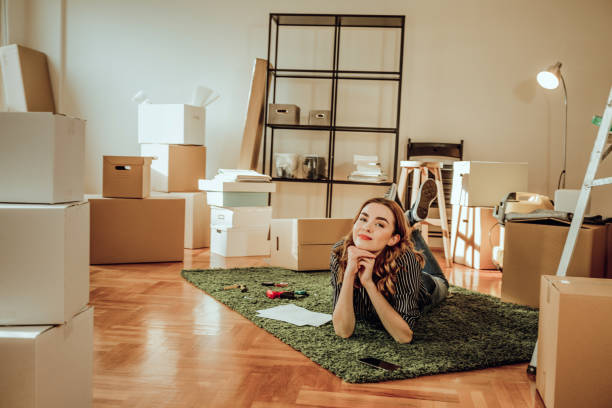 istock Young woman moving to a new apartment. Typing a message while sitting down on a carpet 915917664