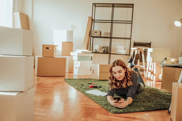 istock Young woman moving to a new apartment. Typing a message while sitting down on a carpet 915917722