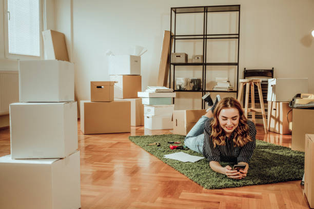 istock Young woman moving to a new apartment. Typing a message while sitting down on a carpet 915917744
