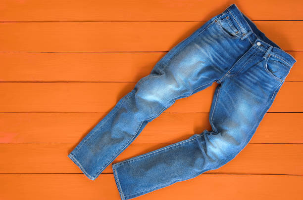 los pantalones del dril de algodón pantalones vaqueros para hombre azul sobre fondo naranja. contraste de color saturado. concepto de ropa de moda. ve desde arriba - pantalón fotografías e imágenes de stock