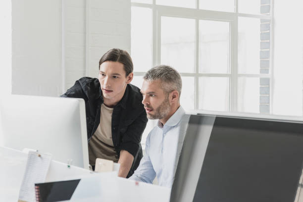 istock Young man and mid adult man looking at computer in office 915933922