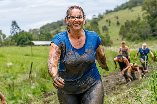 Group of Australian mature women training in a group and competing in a mud run obstacle course