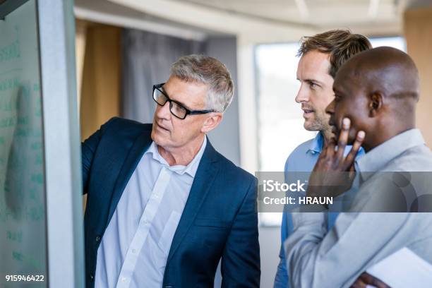 Colleagues Listening To Businessman In Meeting Stock Photo - Download Image Now - Meeting, Whiteboard - Visual Aid, Men