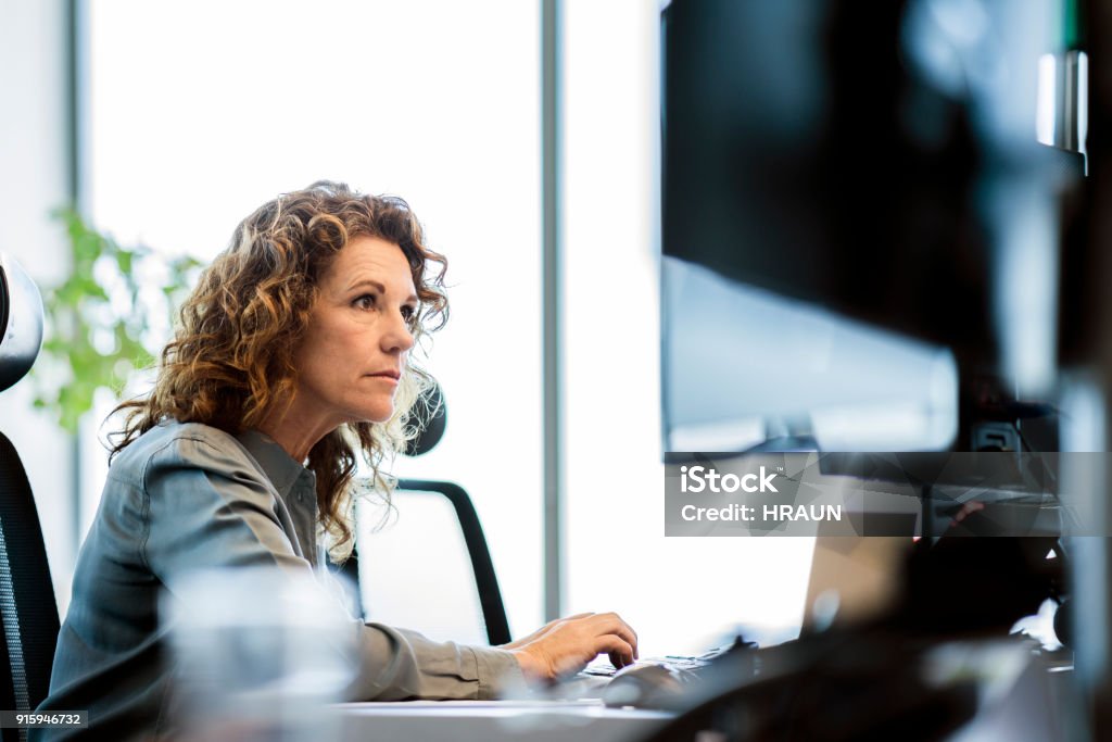 Serious businesswoman using computer at desk Serious mature businesswoman using computer at desk. Female professional is sitting in office. She is wearing smart casuals. Serious Stock Photo