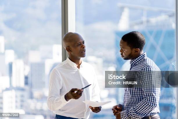 Male Coworkers Discussing Over Document By Window Stock Photo - Download Image Now - Discussion, Two People, Transparent