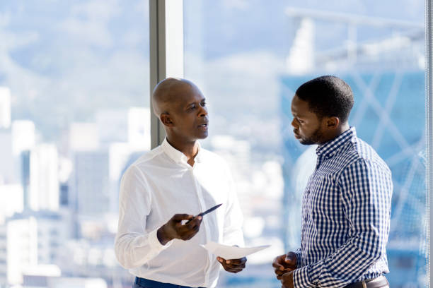 male coworkers discussing over document by window - transparent holding glass focus on foreground imagens e fotografias de stock