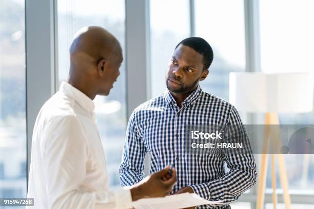 Colleghi Maschi Discutono Su Documento In Ufficio - Fotografie stock e altre immagini di Scambio d'idee - Scambio d'idee, Serio, Due persone