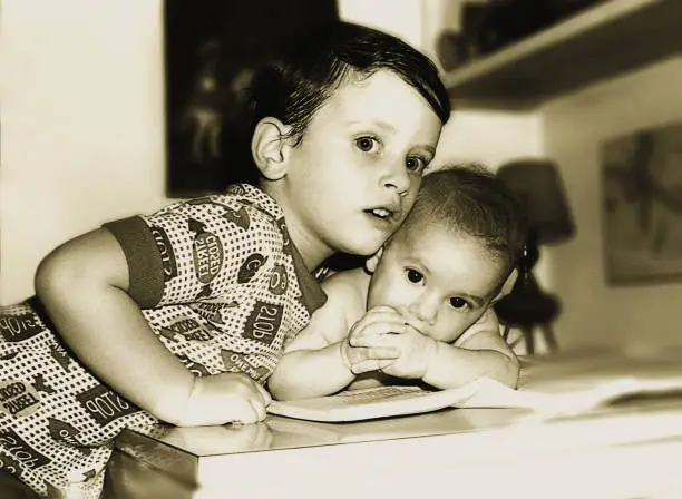 vintage black and white photo from the seventies featuring a boy hugging his new baby sister.