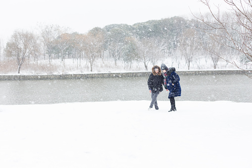 female friends wearing warm clothing cheering in snow at urban park,China.
