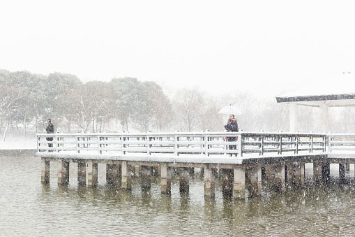 girlfriend holding umbrella on wooden bridge while boyfriend at the side in snow,China.