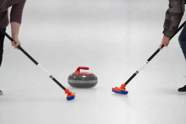 A pair of sweeper lead a red curling stone down the ice