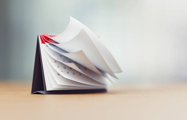 Pages of a red calendar standing over defocused background surface are folding. Horizontal composition with copy space. Calendar and reminder concept with selective focus.