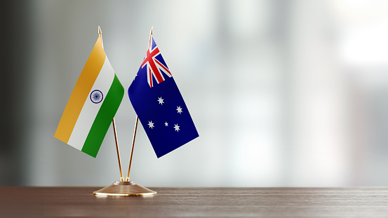 Australian and Indian flag pair on desk over defocused background. Horizontal composition with copy space and selective focus.
