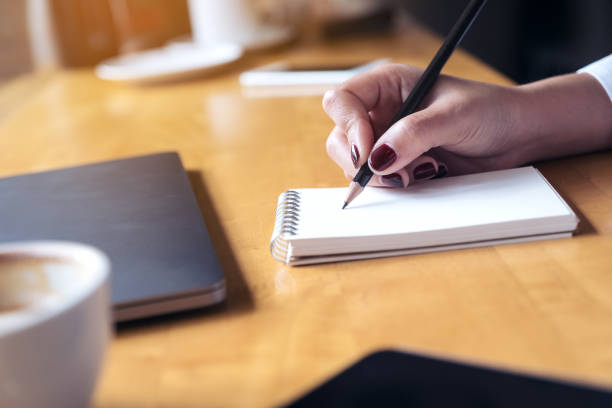 istock Closeup image of woman's hand writing on a blank notebook with laptop , tablet and coffee cup on wooden table background 915986028