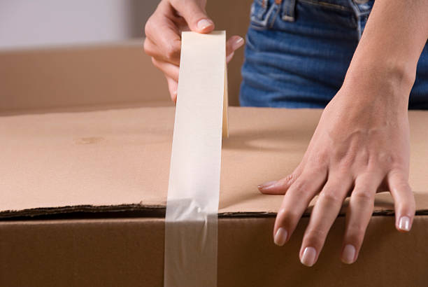 Woman sealing cardboard box with packing tape stock photo