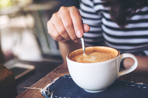 A woman holding coffee spoon and stirring hot coffee on wooden table