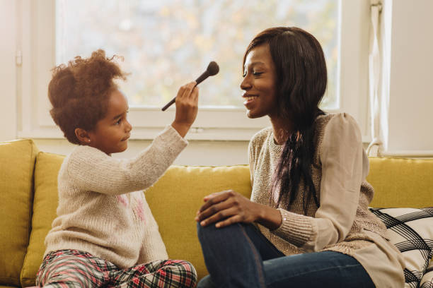 African American little girl applying make-up on her mother at home.