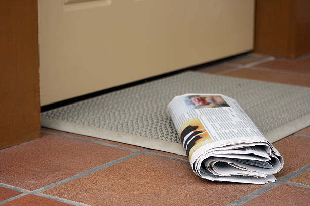 Daily newspaper Daily newspaper waiting to be picked up outside home entrance door. Focus on paper foreground, text blured intentionaly doorstep stock pictures, royalty-free photos & images