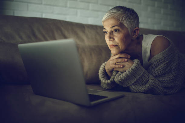 istock Senior woman lying on sofa and watching something on her laptop. 916004236