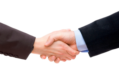 Two unrecognizable caucasian business peoples are shaking hands. One businessperson is wearing gray suit. The other is wearing a black suit.