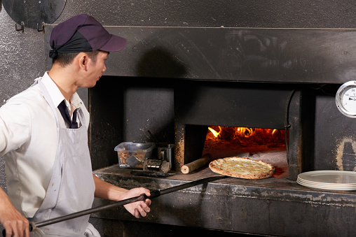Vietnamese cafe worker putting pizza into oven